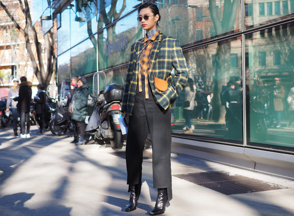 femeie imbracata cu palton in carouri, pantaloni negri si cizme negre inalte